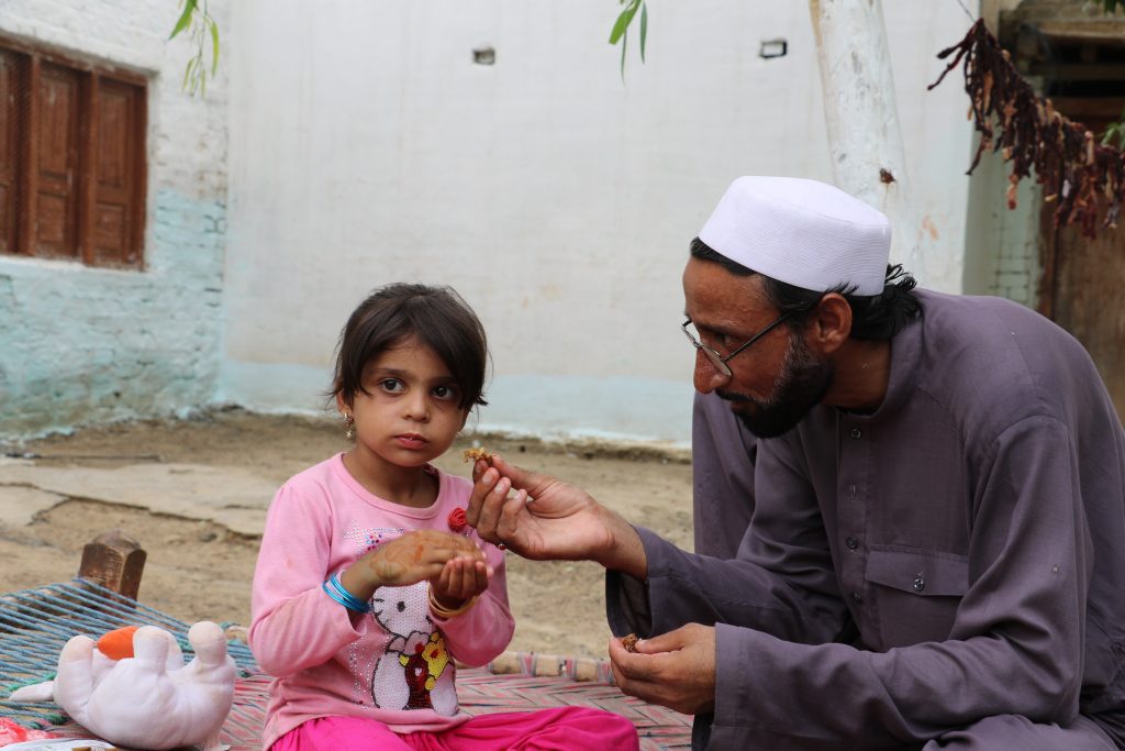 Visually impaired father feeds his daughter from food he received in online qurbani Canada.