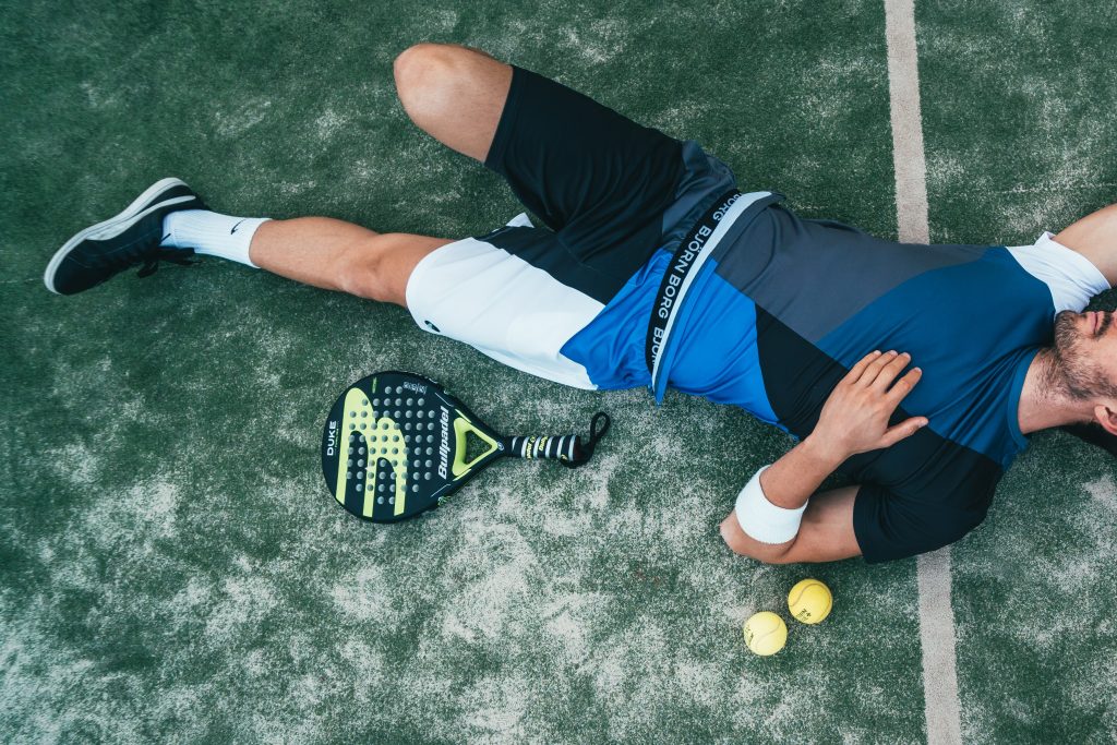 Man lying in tennis court surrounded by tennis racket and balls because fitness not working for mental health during covid