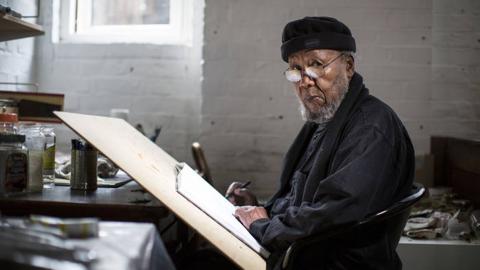 Ibrahim El Salah sits at a desk looking at the camera. His work is a reflection of Islam in Sudan.